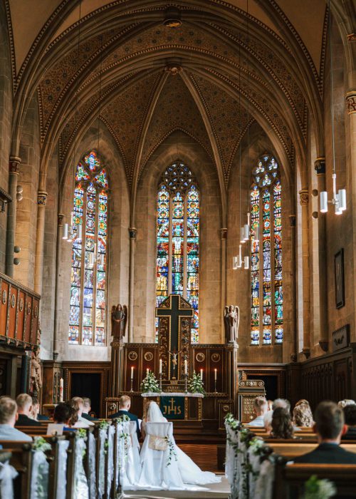 Hochzeit (347) Schön geschmückte Kirche bei der Hochzeit oder Trauung mit dem Brautpaar auf Stühlen und den Gästen auf Bänken mit toller Deko und Kerzen fotografiert von professioneller Fotografin oder Hochzeitsfotografin.